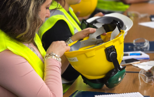 A person in a high-visibility vest sits at a table holding a hard hat