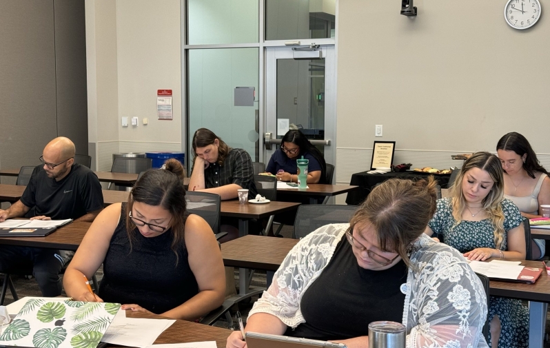 A group of people at classroom desks writing