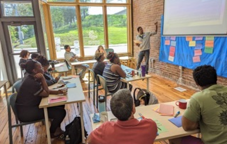 students at desks look up a teacher pointing to a projector