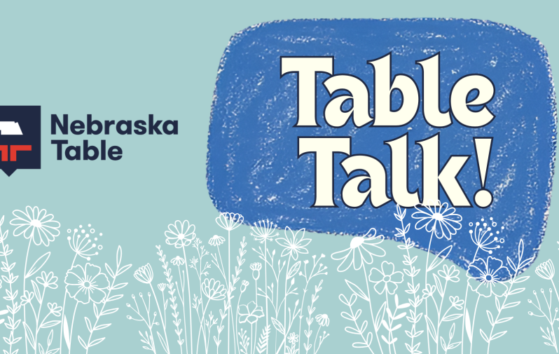 Graphic that reads "Table Talk!" encased inside a blue speech bubble with Nebraska Table logo on left hand side and white outlines of flowers lining bottom of graphic