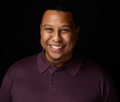 A headshot of a man in a burgundy collared shirt