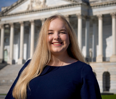 Headshot of a woman with long blonde hair and a black shirt smiling in front of a building with pillars