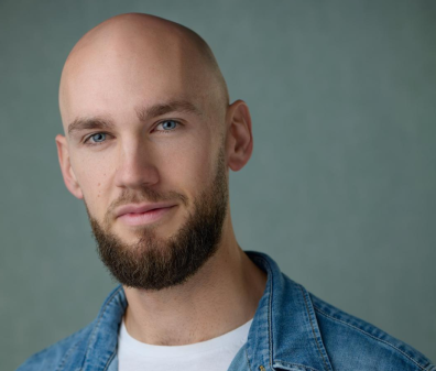 Headshot of a man with a short beard in a white shirt and blue jean jacket