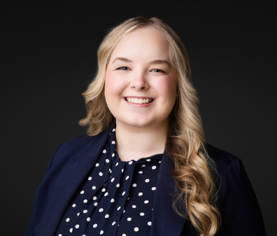 Headshot of a smiling woman with blonde hair wearing a navy shirt with white polka dots and navy blazer