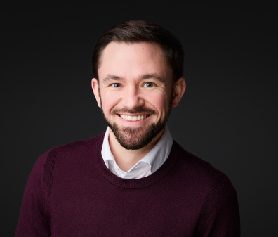 Headshot of a smiling man with a burgundy sweater and white collared shirt