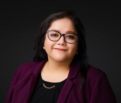 Headshot of a smiling woman with short brown hair, glasses, and a black shirt with a purple blazer