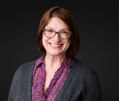 Headshot of a smiling woman with short brown hair, glasses, and a purple shirt with a gray cardigan