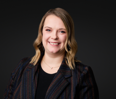 Headshot of a smiling woman with short blonde hair wearing a black shirt and gray plaid blazer 