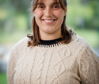 Headshot of a smiling young woman in a tan sweater with short light brown hair