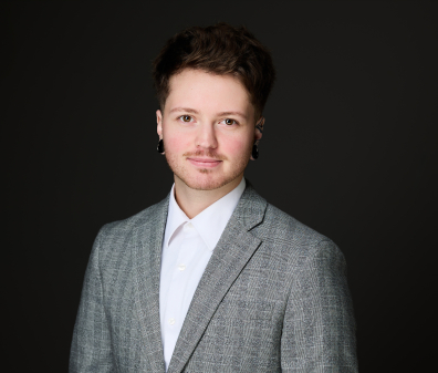 Headshot of a man with brown hair wearing a gray plaid blazer over a white collared shirt