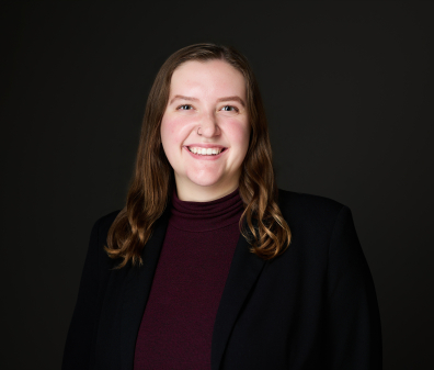 Headshot of a smiling woman with shoulder length brown hair wearing a blazer over a plum turtleneck