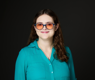 Headshot of a woman with medium length brown hair wearing orange tinted blue glasses and a teal button up shirt